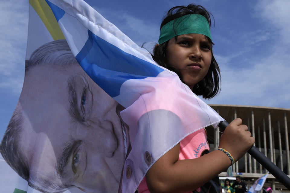 A girl carries a flag with an image of Brazil's President Jair Bolsonaro, who is running for reelection, during a campaign event in Brasilia, Brazil, Saturday, Oct. 29, 2022. Bolsonaro is facing former President Luiz Inacio Lula da Silva in a runoff election set for Oct. 30. (AP Photo/Eraldo Peres)