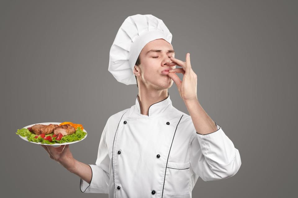 <p>Getty</p> Stock image of young cook in white chef uniform holding a plate with meat dish and making delicious italian gesture over grey background