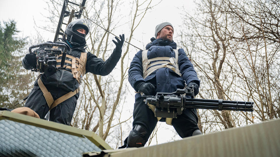 Extraction 2 director Sam Hargrave on top of a train with lead star Chris Hemsworth holding a minigun