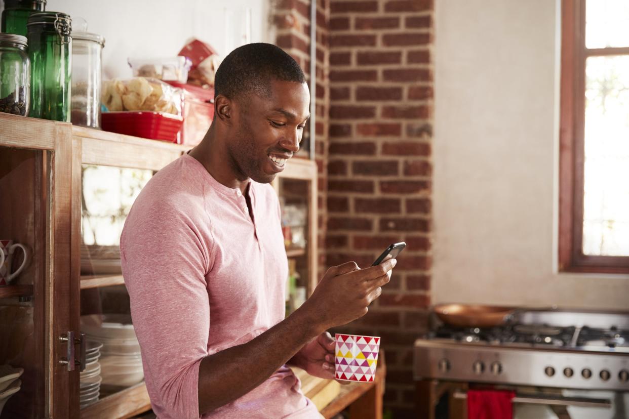Smiling young man in his kitchen on smartphone