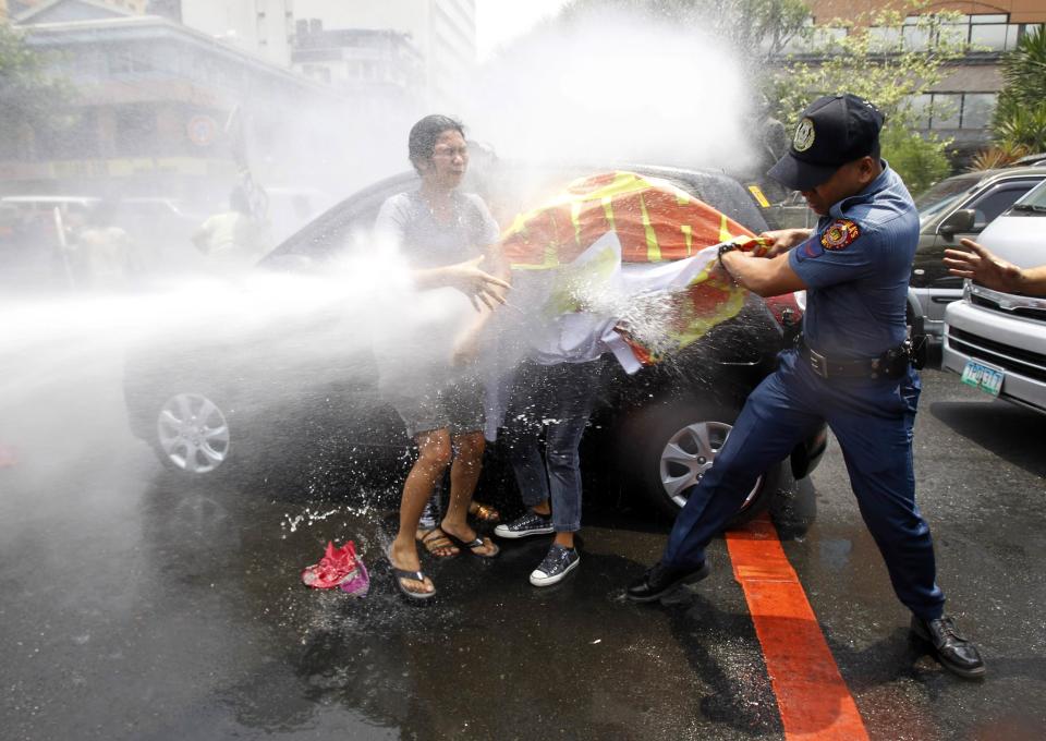 An anti-riot policeman grabs a banner from protesters as they are hit with a water cannon during a protest against the upcoming visit of U.S. President Barack Obama next week, in front of the U.S. embassy in Manila April 23, 2014.