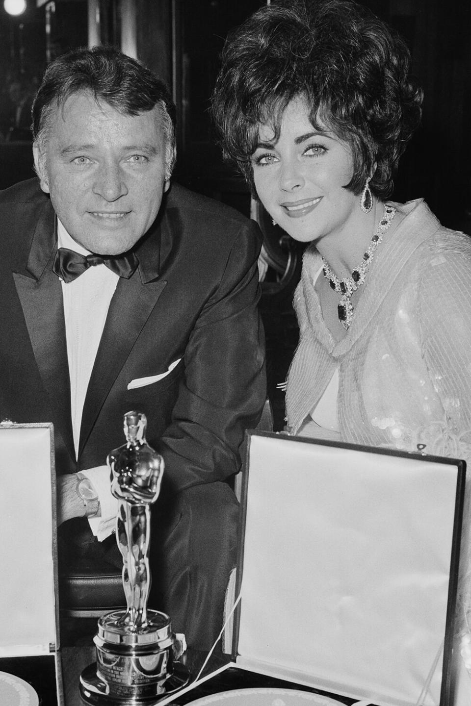 Married actors Elizabeth Taylor (1932 - 2011) and Richard Burton (1925 - 1984) attend the BAFTA Awards dinner at Grosvenor House in London, 26th April 1967. They won the Best British Actress and Best British Actor awards for their roles in 'Who's Afraid of Virginia Woolf?', and Taylor shows off the Academy Award which she won for the same part. Taylor is wearing her Bulgari diamond and emerald necklace. (Photo by Trevor Humphries/Central Press/Getty Images)