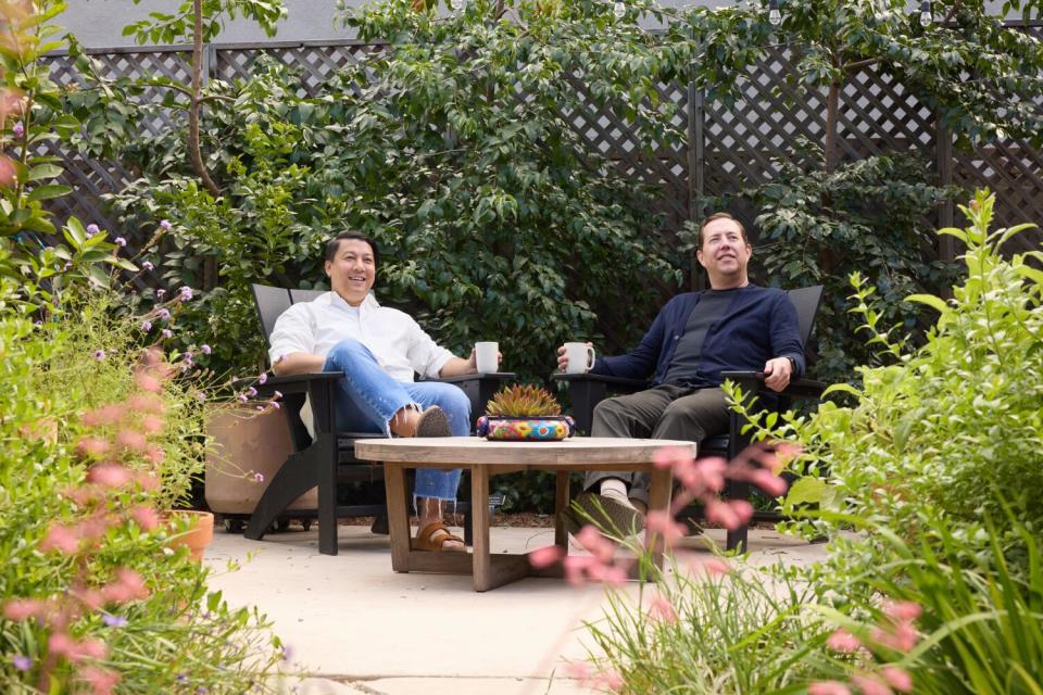 Khoi Pham, left, and Michael Solberg relax in chairs with cups of coffee outside in their leafy backyard.