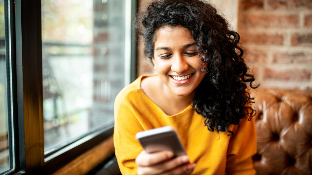 Young Indian woman using mobile phone at the bar.