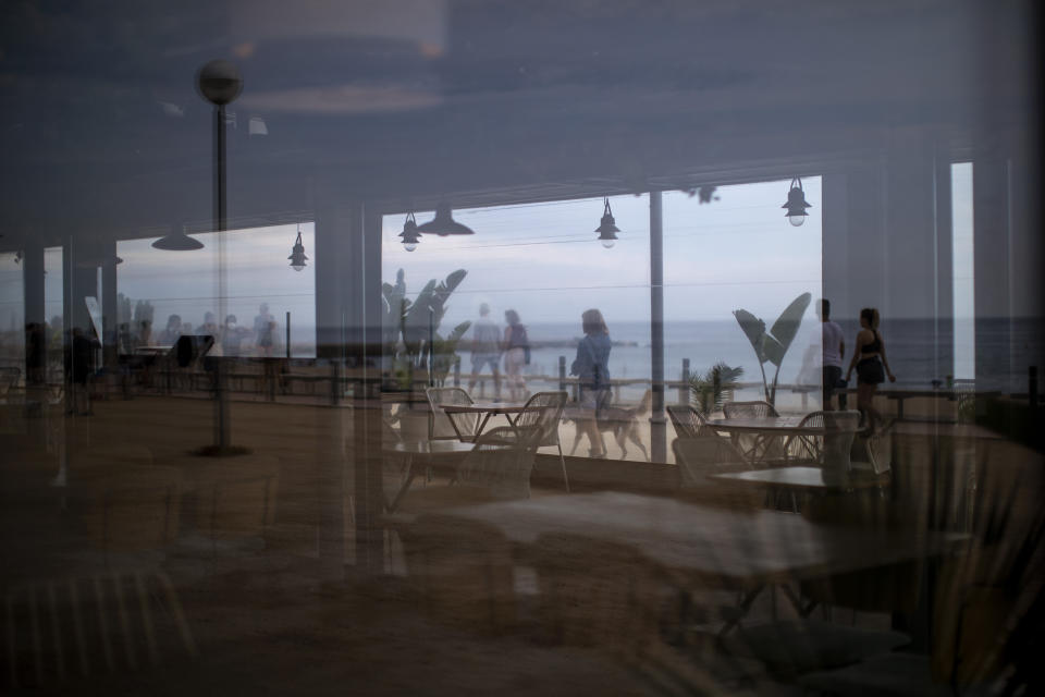 In this Monday, June 1, 2020 photo, local visitors walk past a closed restaurant next to the beach in Barcelona. Spain is waiting until July to reopen its border for foreign tourists. In the meantime, authorities are encouraging Spaniards to vacation inside at home. (AP Photo/Emilio Morenatti)