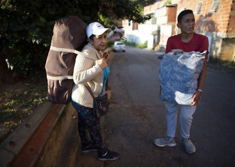 In this Oct. 5, 2019 photo, Daixy Aguero carries duffel bag on her back loaded with beauty products for sale, as she walks with her grandson Joseht Lauser to a market in Caracas, Venezuela. As a teacher Aguero earns the equivalent of roughly $30 a month, which falls short of meeting her grocery list. (AP Photo/Ariana Cubillos)