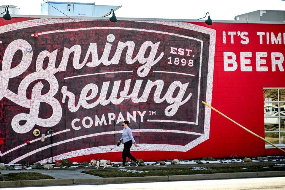 A person walks a dog past a mural outside Lansing Brewing Company on Tuesday, Feb. 20, 2024, in Lansing.