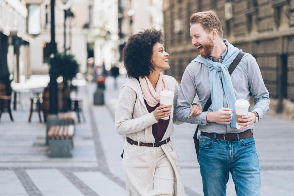 Happy young couple walking on the street drinking coffee and laughing