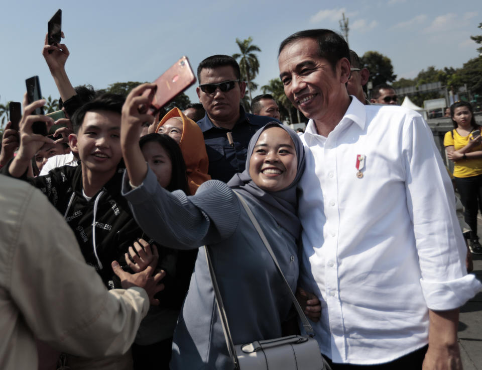 A Muslim woman takes a selfie with Indonesian President Joko Widodo, right, during his visit at the Old Town in Jakarta, Indonesia, Friday, July 26, 2019. Indonesian President Joko Widodo said in an interview Friday that he will push ahead with sweeping and potentially unpopular economic reforms, including a more business-friendly labor law, in his final term because he is no longer constrained by politics. (AP Photo/Dita Alangkara)