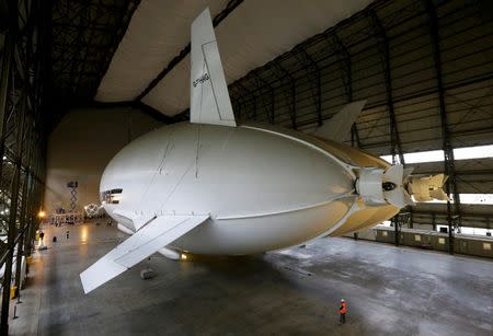 A worker stands under the Airlander 10 hybrid airship during its unveiling in Cardington, Britain March 21, 2016. REUTERS/Darren Staples