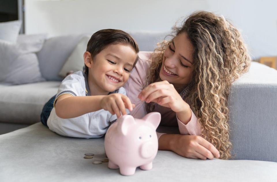 A smiling parent and child are putting coins into a piggy bank.