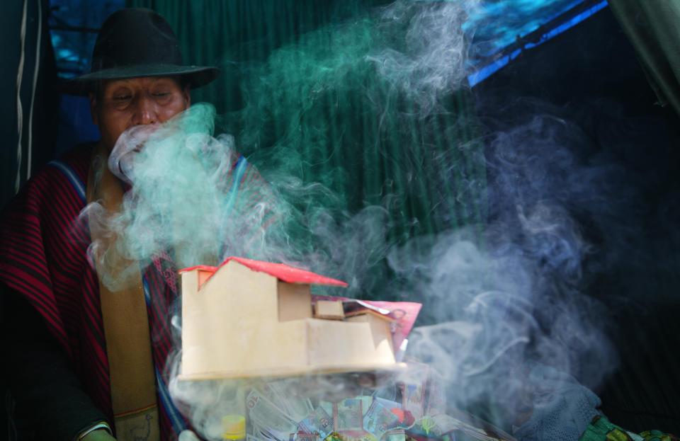 Un brujo indígena aymara bendice miniaturas de una casa y billetes falsos para un cliente durante la feria anual de Alasita en el centro de La Paz, Bolivia, el miércoles 24 de enero de 2024. En el día de inauguración de la feria se ofrecen réplicas en miniatura de las cosas que las personas anhelan o desean, como casas, vehículos o salud, para que se conviertan en realidad. Alasita es una palabra aymara que significa "cómprame". (AP Foto/Juan Karita)