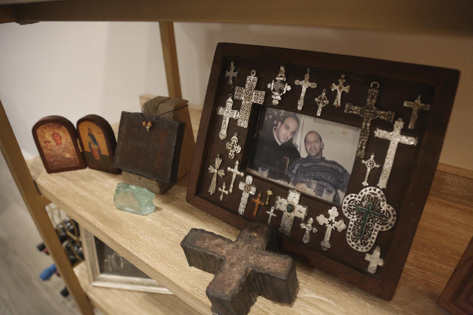 A photo of Anthoula Katsimatides' brothers John, left, and Michael Katsimatides, right, who died just one year apart from each other, sits on a shelf beside a cross fashioned from the steel of the fallen World Trade Center on Monday, Aug. 30, 2021, in the Queens borough of New York. John often visited the old St. Nicholas Greek Orthodox Church to say a prayer and light a candle as he went to or from work nearby on the 104th floor of the World Trade Center's north tower. The church stood as a quiet oasis amid the soaring financial district. (AP Photo/Jessie Wardarski)