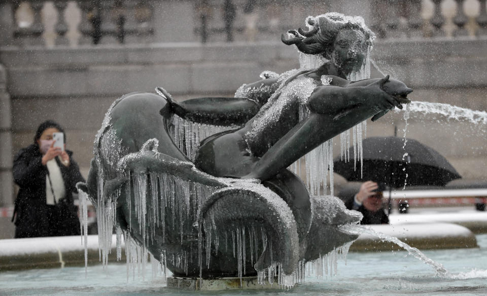 People photograph icicles on the fountain in Trafalgar Square as temperatures dropped below freezing in London, Monday, Feb. 8, 2021. Snow has swept across the country, with further snowfall predicted, bringing travel problems as temperatures dropped. (AP Photo/Kirsty Wigglesworth)