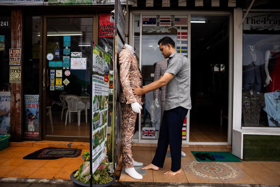 A man adjusts a headless mannequin in a brown patterned suit in a store