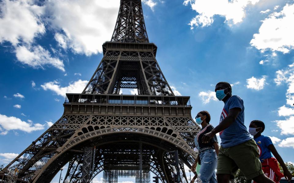 A family on holiday wearing protective face masks walk near the Eiffel Tower, in Paris, France - IAN LANGSDON/Shutterstock