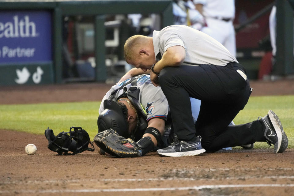 Miami Marlins catcher Payton Henry gets looked at by the trainer after getting hit with a foul ball against the Arizona Diamondbacks in the first inning during a baseball game, Tuesday, May 10, 2022, in Phoenix. (AP Photo/Rick Scuteri)
