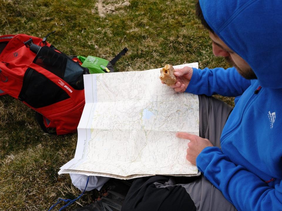 Joshua Kian sitting on the ground and pointing at a map with one hand while holding food in the other.