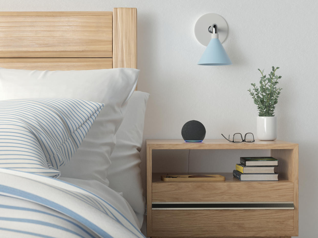  A black Amazon Echo smart speaker on a wooden nightstand next  to a bed. 