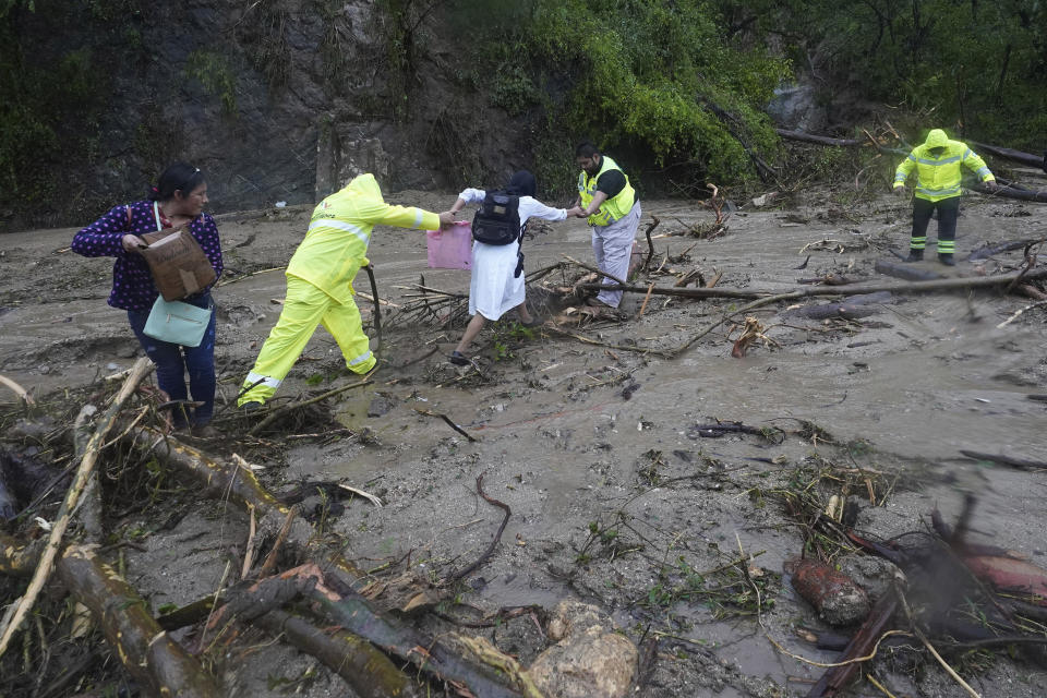 FILE - A woman is helped across a highway blocked by a landslide triggered by Hurricane Otis, near Acapulco, Mexico, Oct. 25, 2023. October was the fifth straight month that Earth set a record for the hottest month in recorded history. (AP Photo/Marco Ugarte, File)