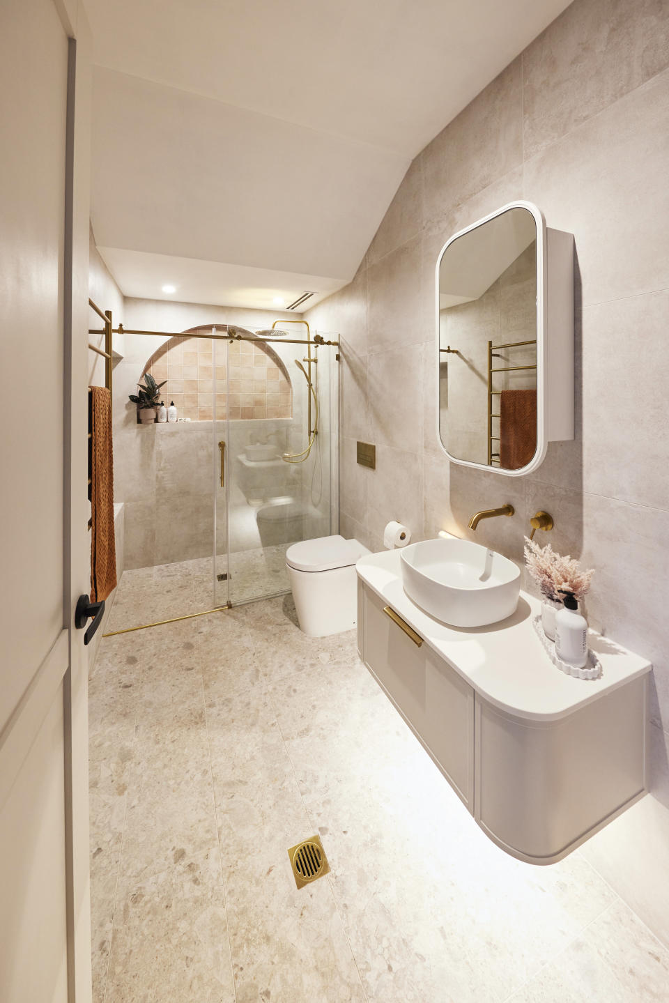 A long shot of the cream coloured bathroom with the vanity and shower. 