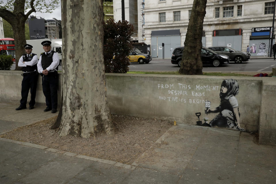 British police officers stand near a new piece of street art that people noticed for the first time last night and is believed to be by street artist Banksy on a wall where Extinction Rebellion climate protesters had set up a camp in Marble Arch, London, Friday, April 26, 2019. Extinction Rebellion ended its remaining blockades in London on Thursday evening with a closing ceremony, after disrupting the British capital for 10 days. The non-violent protest group is seeking negotiations with the government on its demand to make slowing climate change a top priority. (AP Photo/Matt Dunham)