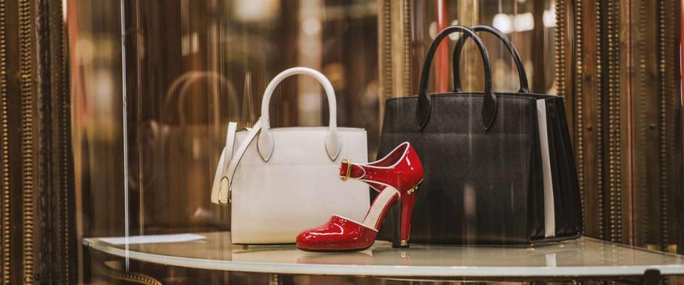 Two designer bags and a pair of shoes sit on a table in a shop.