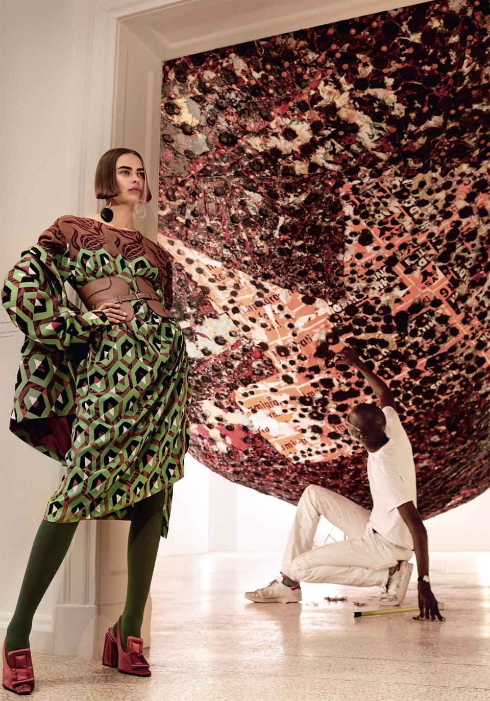 <strong>Culture Clash</strong> A gorgeous riot of earthy terra-cotta neutrals stands out starkly against Mark Bradford’s <em>Spoiled Foot</em> inside the United States Pavilion. Dries Van Noten jacket ($1,975) and dress ($1,005). Jacket at Bergdorf Goodman, NYC. Dress at Barneys New York, NYC. Simon Miller earring. Tod’s belt. Falke tights. Marni shoes.