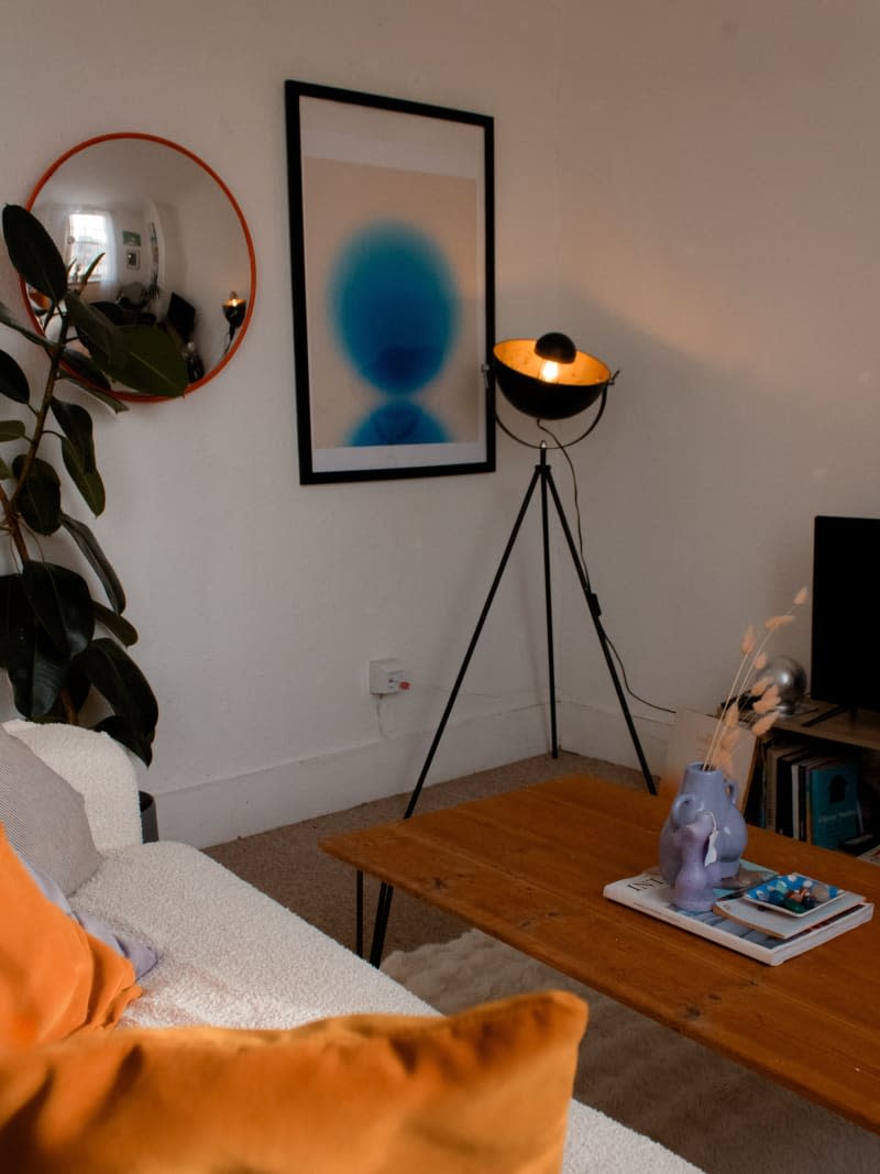 A modern tripod lamp next to a framed piece of art.