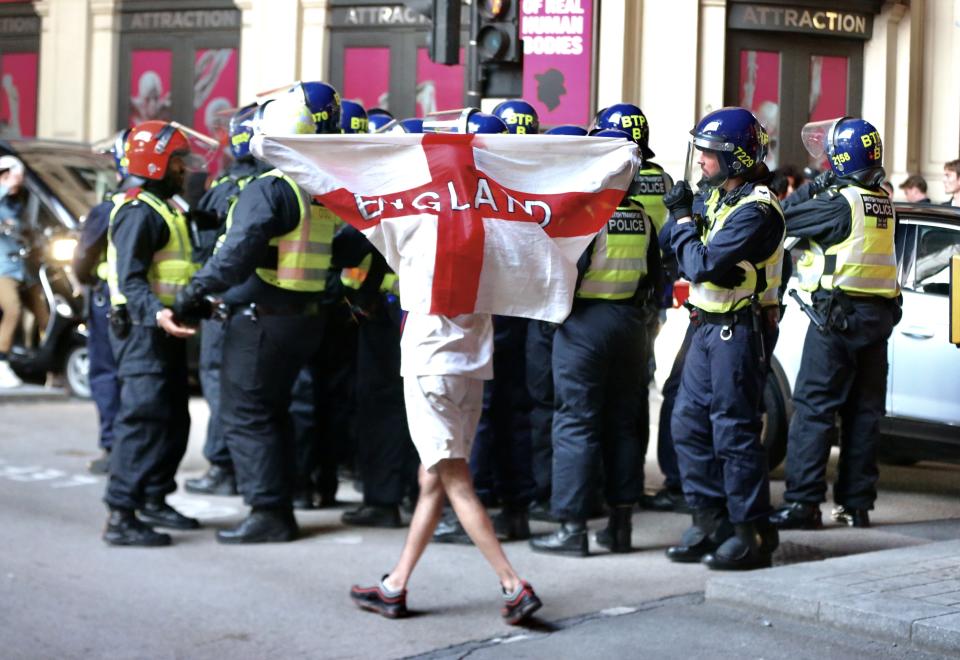 An England fan drapes himself with a flag as he walks past police at Piccadilly Circus in London.