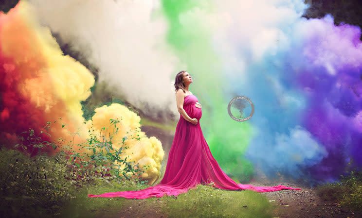 Pregnant woman stands in reverie against a background of rainbow colored smoke