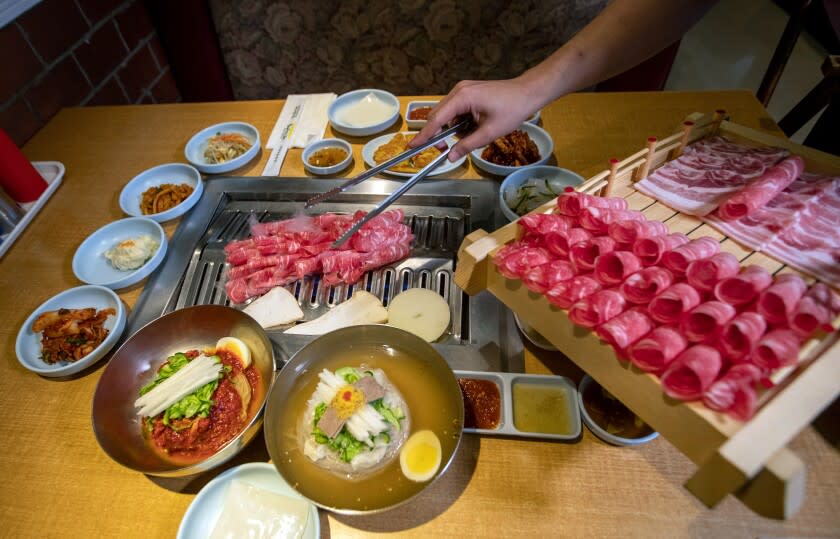 GARDEN GROVE, CALIF. -- WEDNESDAY, NOVEMBER 20, 2019: Korean BBQ beef brisket is cooked at the table at Mo Ran Gak Korean B.B.Q. in Garden Grove, Calif., on Nov. 20, 2019. In foreground is NK-style Bibbim Naengmyeon, left, and Moon Naengmyeon at right. (Allen J. Schaben / Los Angeles Times)
