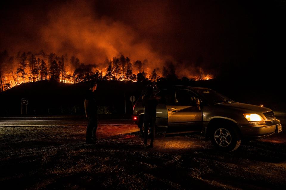 People watch the Glass Fire from the side of the road and the flames make their way down the hill near Calistoga on Monday. 