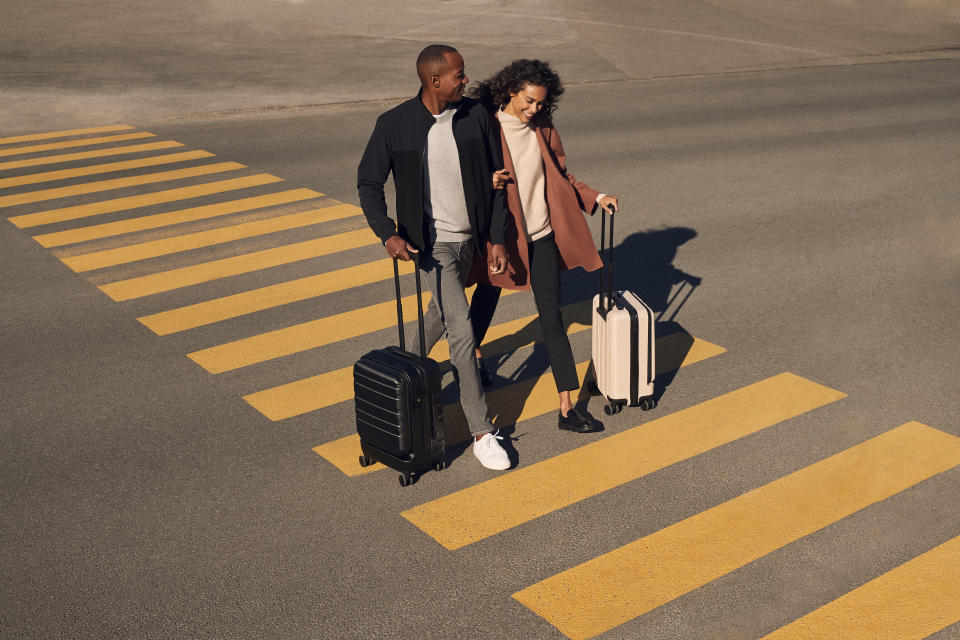 A couple walks along a crosswalk wheeling their carry-on suitcases