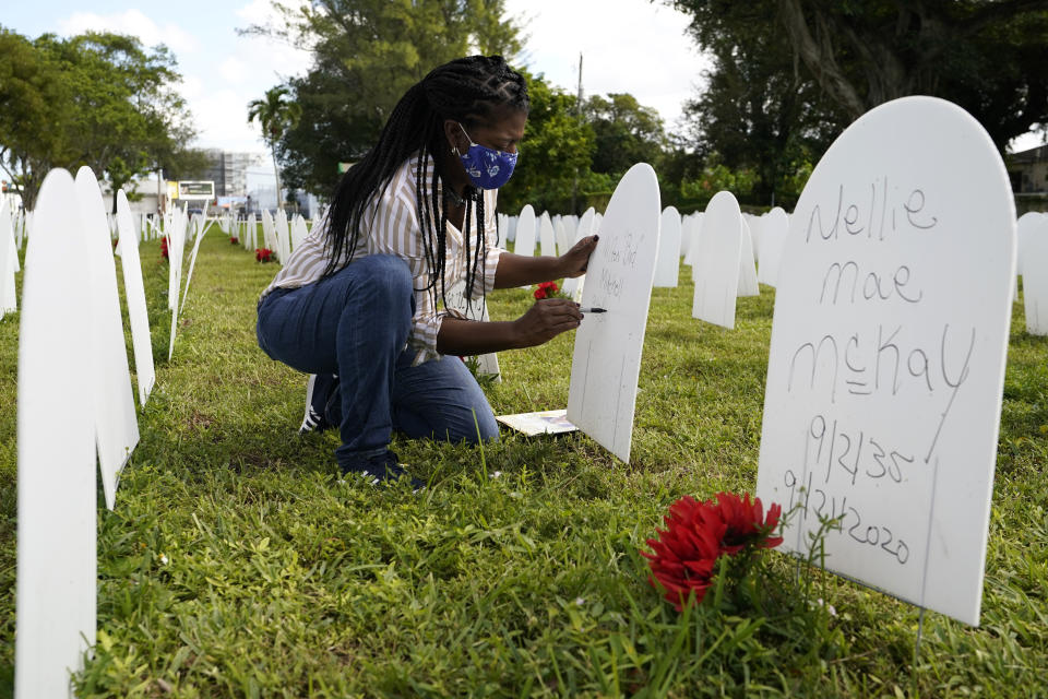 FILE - In this Nov. 24, 2020, file photo, Joanna Moore writes a tribute to her cousin Wilton "Bud" Mitchell who died of COVID-19 at a symbolic cemetery created to remember and honor lives lost to COVID-19, in the Liberty City neighborhood of Miami. The U.S. death toll from COVID-19 has topped 600,000, even as the vaccination drive has drastically slashed daily cases and deaths and allowed the country to emerge from the gloom. (AP Photo/Lynne Sladky, File)