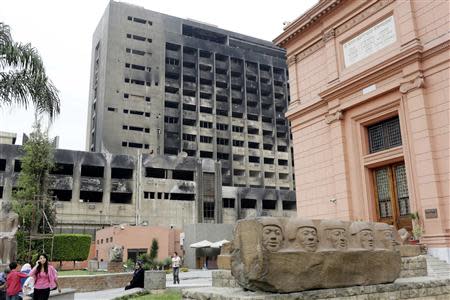 People stand and walk near the dissolved National Democratic Party (NDP) building of Egypt's former President Hosni Mubarak, which was partially burnt down during the January 25 Revolution, with the Egyptian Museum seen on the right, in Cairo April 19, 2014. REUTERS/Asmaa Waguih