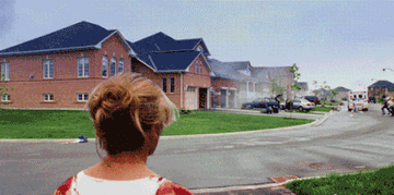 A bloodied woman on suburban street watches people run and smoke rise in the distance