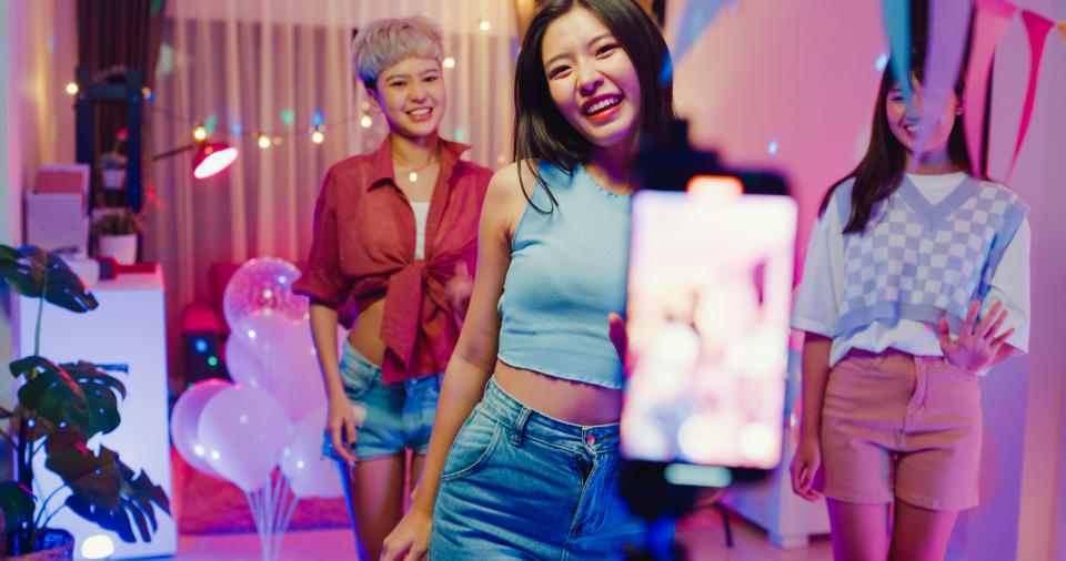 Young Asian female friends tiktok created her dancing video by smartphone having fun at colorful house party at night. Lifestyle together concept.