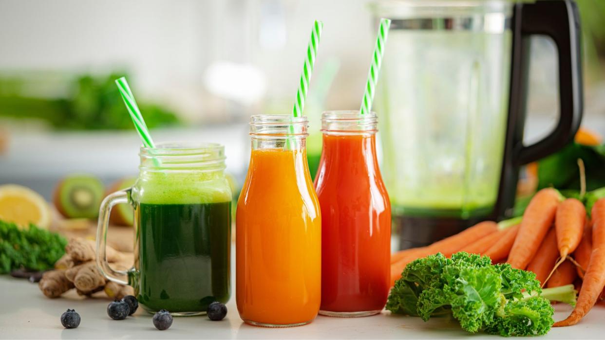  Some glass jars with smoothies in front of a blender 