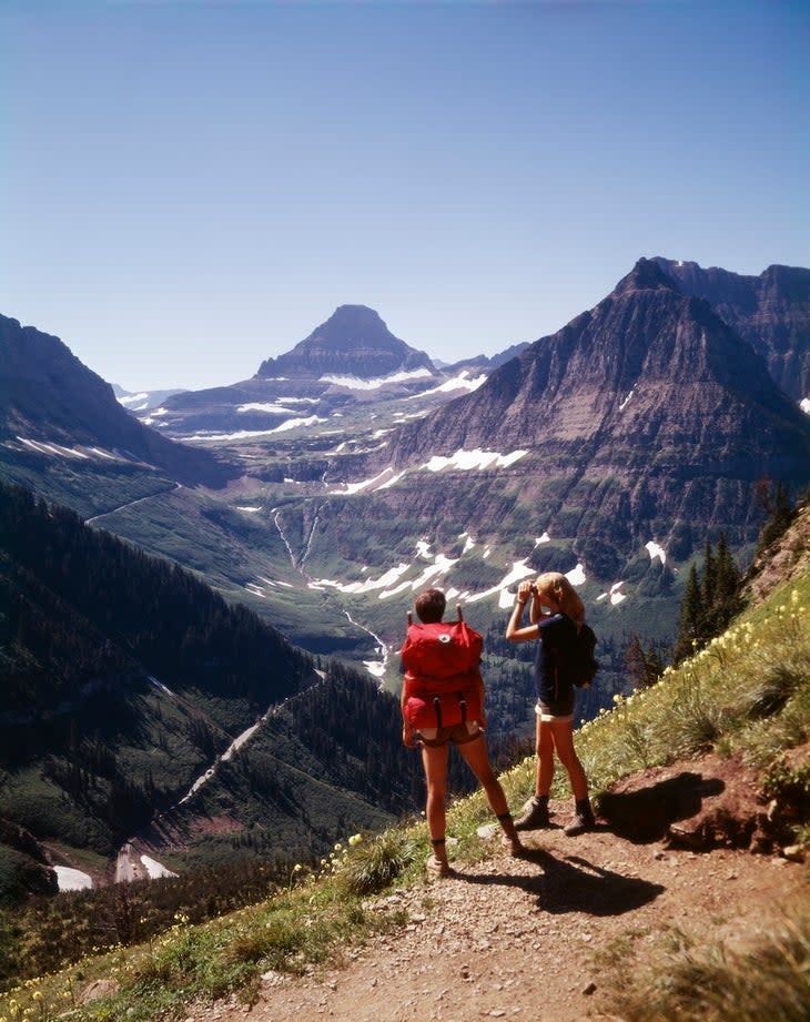 1970s BACK VIEW OF TWO HIKERS ONE MAN ONE WOMAN ON GRANITE PARK TRAIL LOOKING AT VIEW GLACIER NATIONAL PARK MONTANA