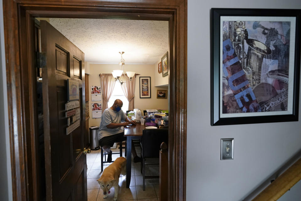 Larry Brown sits at the kitchen table at his parents house, Thursday, Aug. 27, 2020, in Indianapolis. Recovering from COVID-19, Brown still has to stretch his hands and legs, which stiffen up frequently. (AP Photo/Darron Cummings)