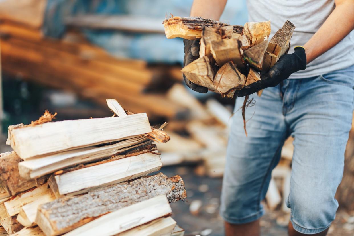 A pile of stacked firewood, prepared for heating the house. Gathering fire wood for winter or bonfire. Man holds fire wood in hands.