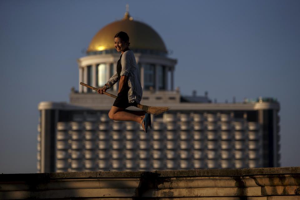 A visitor jumps with a broom on an unfinished structure of an abandoned building in Bangkok