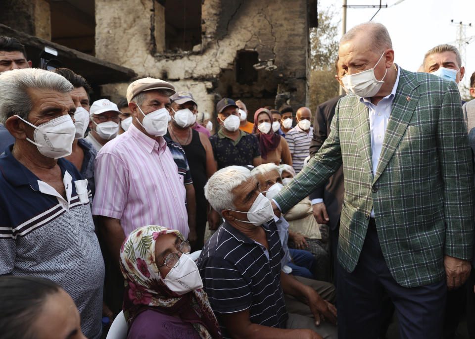 Turkey's President Recep Tayyip Erdogan speaks with villagers in front of a wildfire-destroyed house in Manavgat, Antalya, Turkey, Saturday, July 31, 2021. The death toll from wildfires raging in Turkey's Mediterranean towns rose to six Saturday after two forest workers were killed, the country's health minister said. Fires across Turkey since Wednesday burned down forests, encroaching on villages and tourist destinations and forcing people to evacuate.(Turkish Presidency via AP, Pool)
