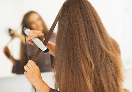 Woman straightening hair with straightener (iStock)