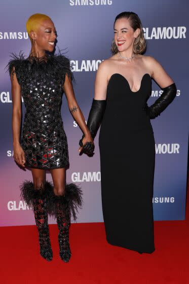 Samira Wiley smiling and holding hands with Lauren Morelli both wearing black dresses on red carpet
