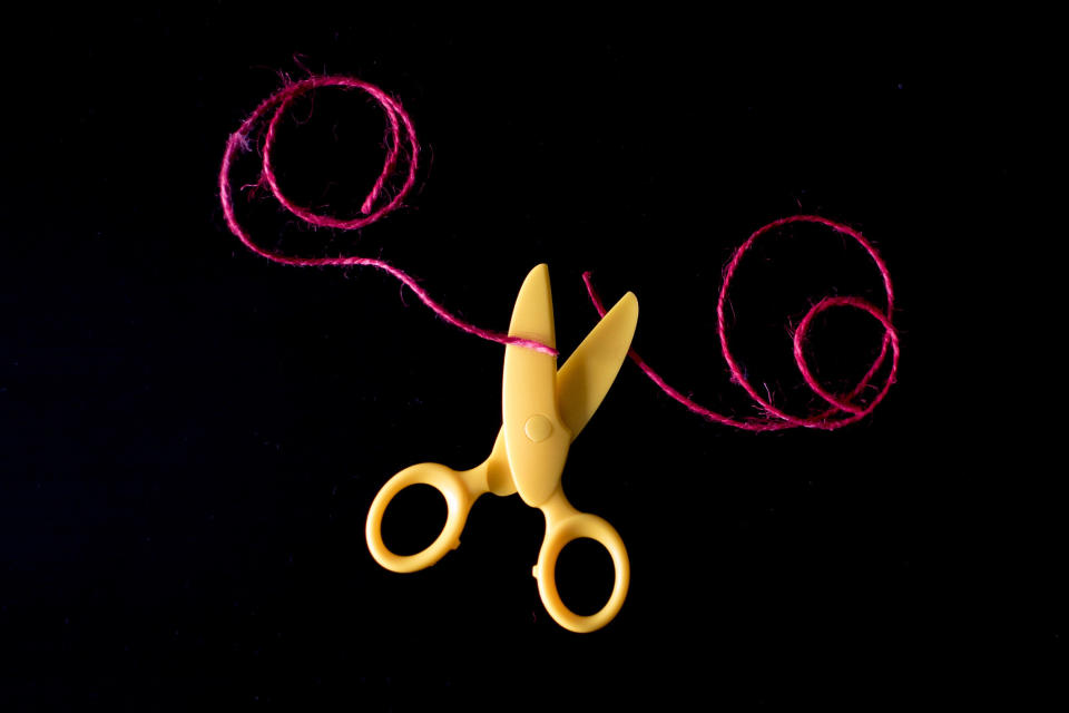 A stock image of a pair of toy scissors cutting a thread