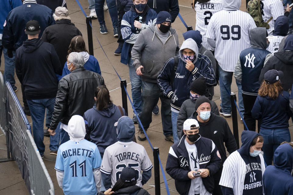 Spectators wait on a security line outside Yankee Stadium before an opening day baseball game against the Toronto Blue Jays, Thursday, April 1, 2021, in the Bronx borough of New York. Fans are back at the ballpark in limited numbers after they were shut out completely during the regular season last year due to the COVID-19 pandemic.(AP Photo/John Minchillo)