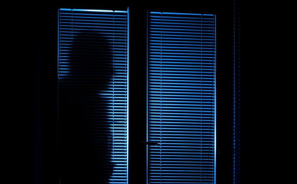 Silhouette of a person outside of a door with blinds closed at night