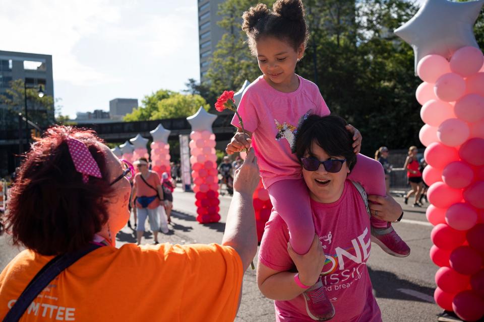 April Johnson, of Reynoldsburg, a breast cancer survivor, holds her 4-year-old daughter, Emerson, on her shoulder as she receives a flower Saturday at the annual Komen Columbus Race for the Cure, which is back in person, after a two-year absence because of COVID-19.